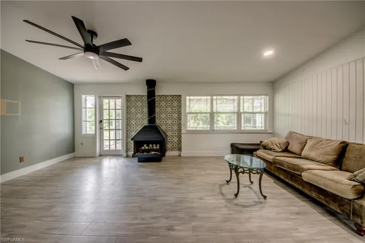 Living room with a wood stove, wood finished floors, ceiling fan, and lofted ceiling