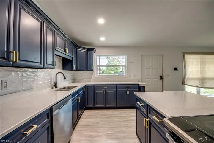Kitchen featuring stainless steel appliances, tasteful backsplash, light wood-style floors, blue cabinets, and light stone countertops