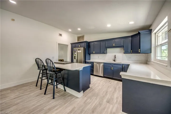 Kitchen with stainless steel appliances, blue cabinetry, a kitchen breakfast bar, backsplash, and light countertops