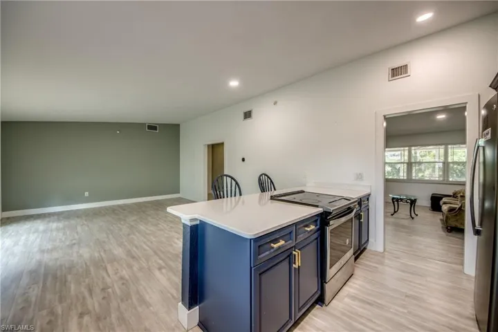 Kitchen with electric range, blue cabinets, freestanding refrigerator, light wood finished floors, and recessed lighting
