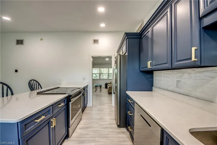 Kitchen featuring stainless steel appliances, blue cabinetry, decorative backsplash, light wood finished floors, and light stone counters