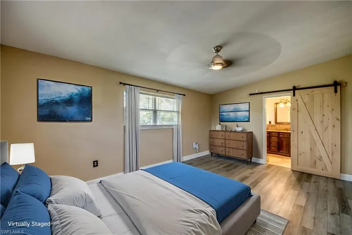 Bedroom with a barn door, light wood-style floors, vaulted ceiling, ensuite bath, and a ceiling fan