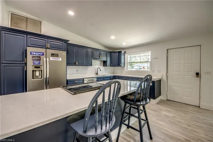 Kitchen featuring appliances with stainless steel finishes, vaulted ceiling, a breakfast bar area, decorative backsplash, and recessed lighting