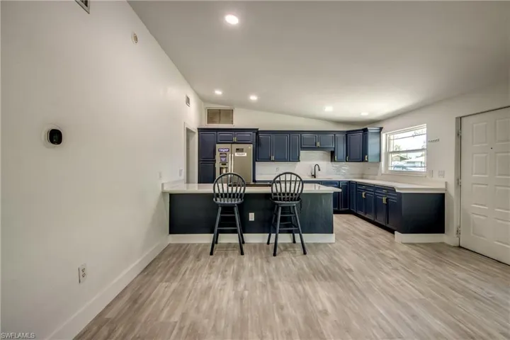 Kitchen featuring blue cabinets, stainless steel refrigerator with ice dispenser, a peninsula, a breakfast bar area, and backsplash