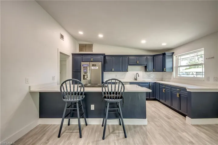 Kitchen with stainless steel fridge with ice dispenser, a peninsula, a kitchen bar, blue cabinets, and lofted ceiling