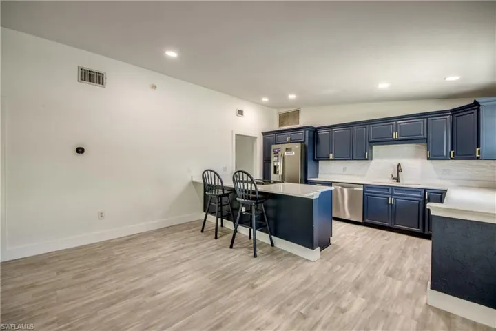 Kitchen featuring stainless steel appliances, a kitchen bar, light countertops, blue cabinets, and tasteful backsplash