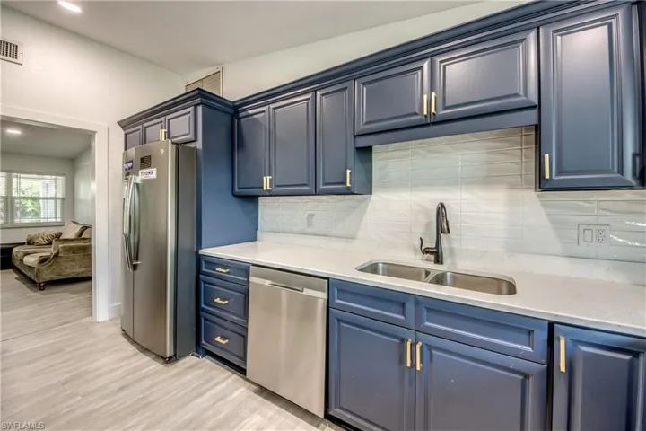 Kitchen with appliances with stainless steel finishes, blue cabinetry, tasteful backsplash, and light wood-type flooring