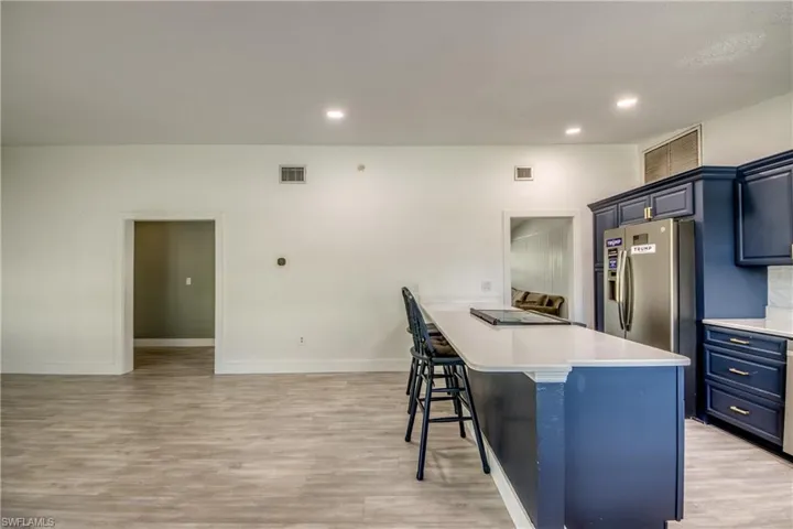 Kitchen with freestanding refrigerator, a kitchen bar, light wood-type flooring, blue cabinetry, and recessed lighting