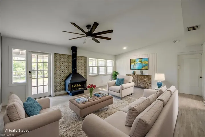 Living area featuring a wood stove, ceiling fan, lofted ceiling, and light wood-style flooring