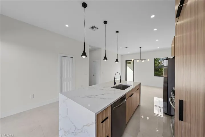 Kitchen featuring light stone counters, modern cabinets, a large island with sink, stainless steel appliances, and decorative light fixtures