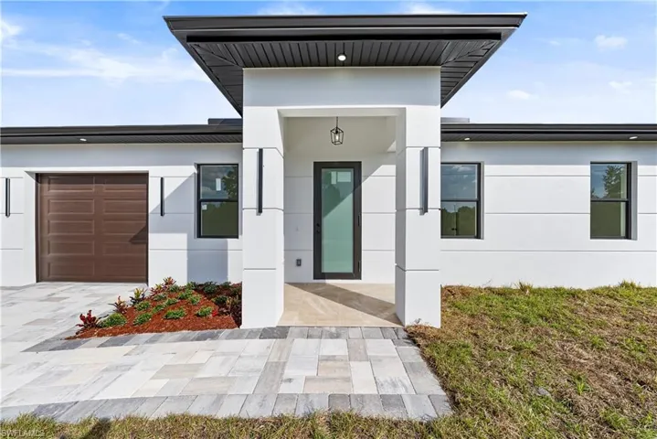 Entrance to property with stucco siding, a garage, covered porch, and driveway