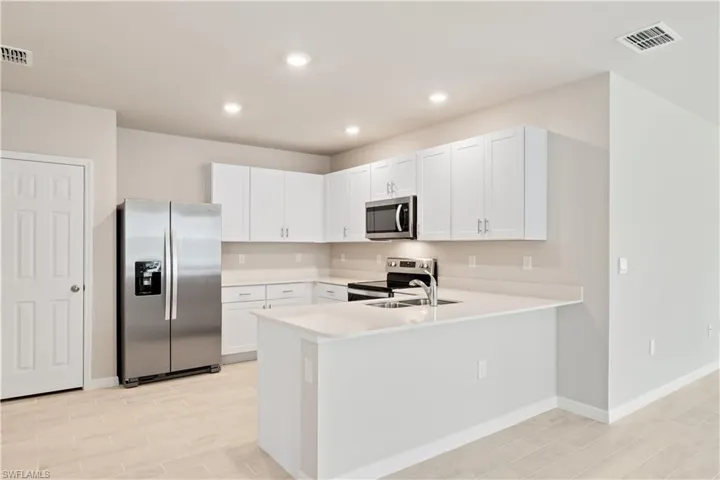 Kitchen with light hardwood / wood-style flooring, white cabinetry, sink, kitchen peninsula, and stainless steel appliances