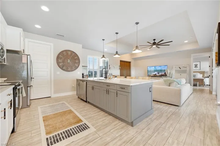 Kitchen with gray cabinetry, a kitchen island with sink, sink, a tray ceiling, and white cabinetry