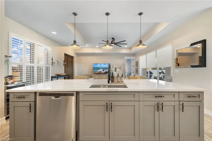 Kitchen with sink, stainless steel dishwasher, a tray ceiling, decorative light fixtures, and light stone counters