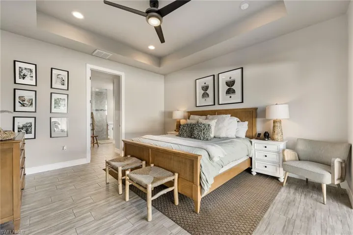 Bedroom with ceiling fan, a raised ceiling, and connected bathroom