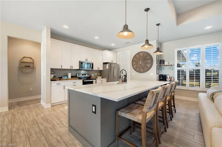Kitchen featuring light stone counters, decorative light fixtures, a kitchen bar, white cabinets, and appliances with stainless steel finishes