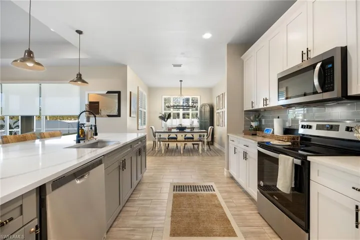 Kitchen featuring white cabinetry, sink, hanging light fixtures, light stone counters, and appliances with stainless steel finishes