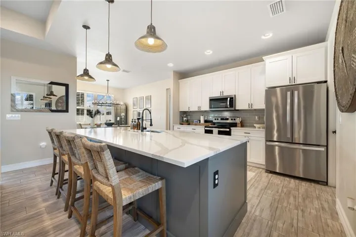 Kitchen featuring a large island with sink, white cabinets, light stone countertops, appliances with stainless steel finishes, and decorative light fixtures
