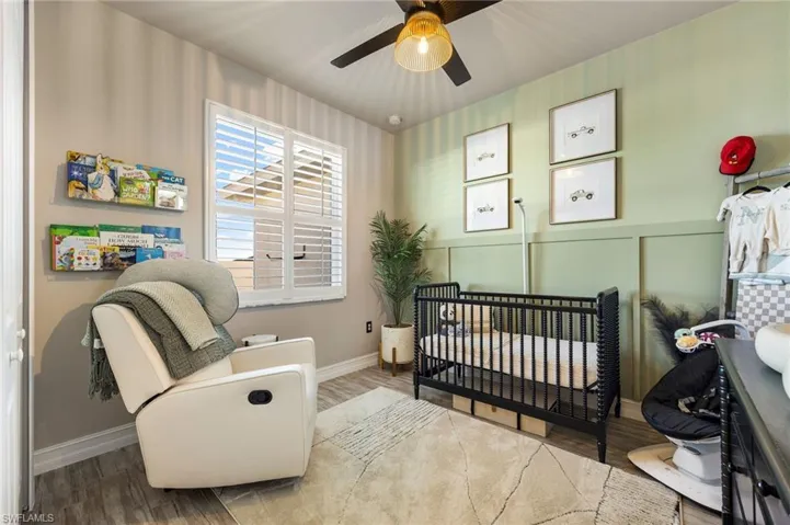 Bedroom with hardwood / wood-style flooring, ceiling fan, and a crib