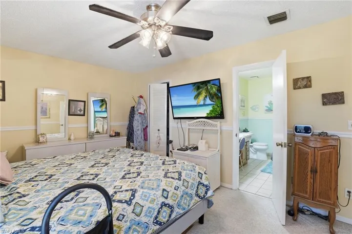 Primary Bedroom with ensuite bathroom, light carpet, a ceiling fan