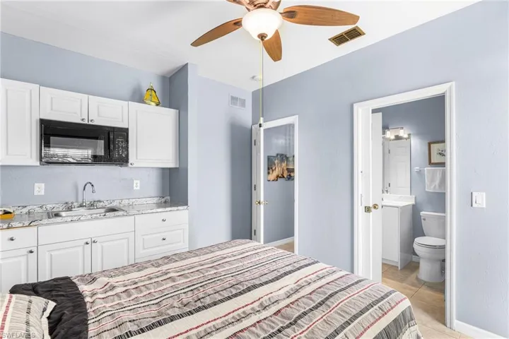 Kitchenette featuring white cabinetry, a built-in microwave, and a stainless steel sink with a stone-finish countertop