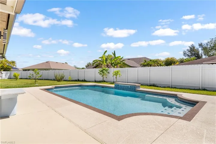 Expansive backyard featuring a rectangular swimming pool with integrated steps, a decorative water feature with blue mosaic tile, and a spacious concrete patio