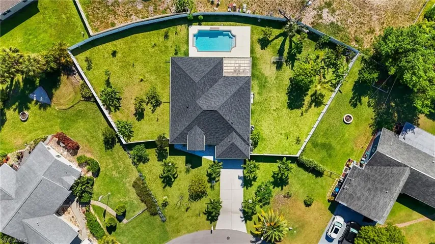 Expansive property featuring a central home with a dark shingle roof, a private swimming pool, a concrete driveway, and mature landscaping
