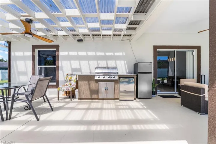 Covered patio featuring a slatted translucent roof, a built-in outdoor grill station with integrated cabinetry and a countertop, and a ceiling fan