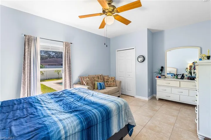 Room featuring tile flooring, a window overlooking a fenced yard, a ceiling fan with light fixture, and a bi-fold closet door