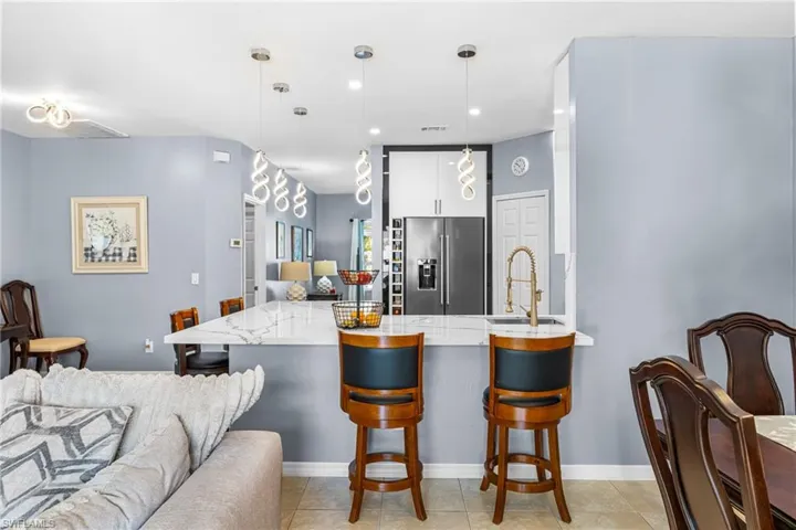 Open-concept kitchen featuring a white marble-finish countertop, stainless steel refrigerator, and a gold-finish pull-down faucet