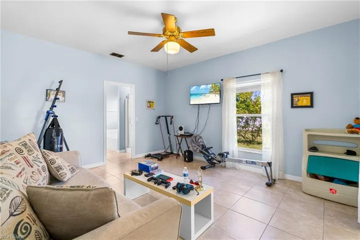 Spacious room featuring neutral tile flooring, light blue wall finishes, a ceiling fan, a prominent window, and an interior doorway