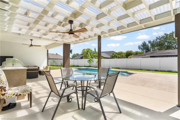 Expansive covered patio featuring a translucent ceiling, dual ceiling fans, built-in outdoor kitchen with grill, and a inground pool