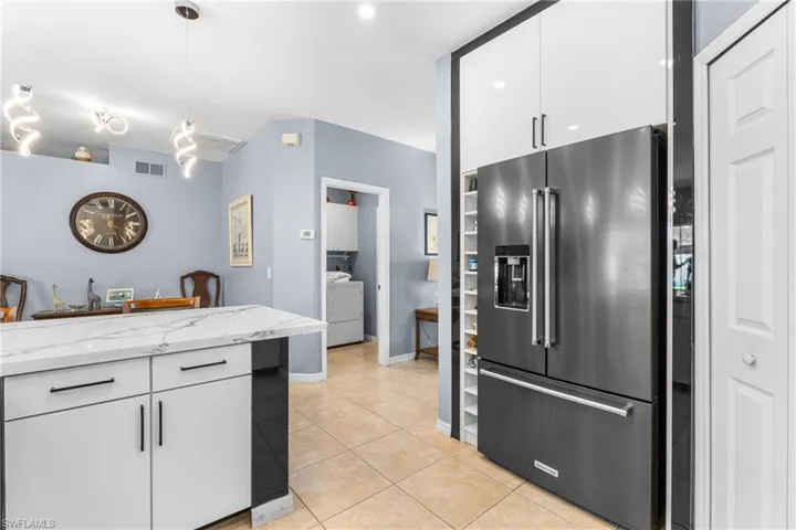 Kitchen featuring a stainless steel French door refrigerator, white upper cabinetry, and a kitchen island with a white countertop