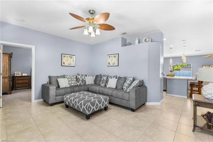 Living area featuring neutral tile flooring, a ceiling fan with integrated lighting, and a partial wall opening to the kitchen