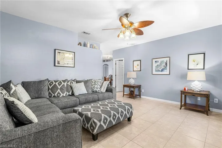 Spacious living area featuring light-toned tile flooring, light blue walls, and a ceiling fan with integrated lighting