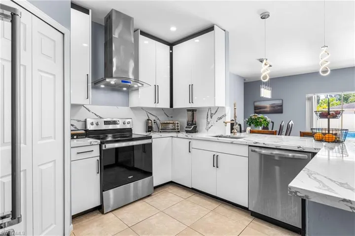 Modern kitchen featuring white cabinetry, stone-finish countertops, and stainless steel appliances including a range, dishwasher, and range hood