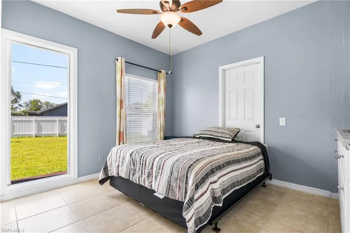 Spacious room featuring tile flooring, a large window offering backyard access, an additional window with blinds, a ceiling fan with integrated lighting, and a built-in cabinet with a light-colored countertop