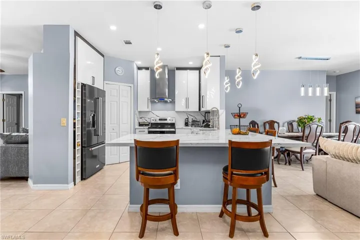 Open-concept kitchen featuring an island with a light-toned countertop, a range with a hood, a dark-finish refrigerator, and contrasting light and dark cabinetry