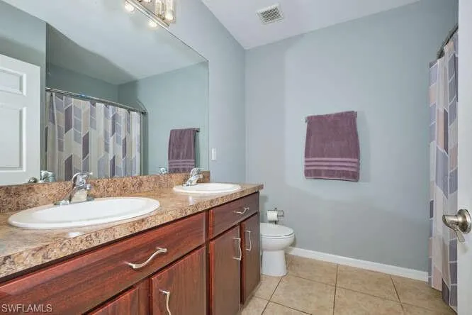 Full bathroom with a shower with shower curtain, double vanity, and light tile patterned flooring