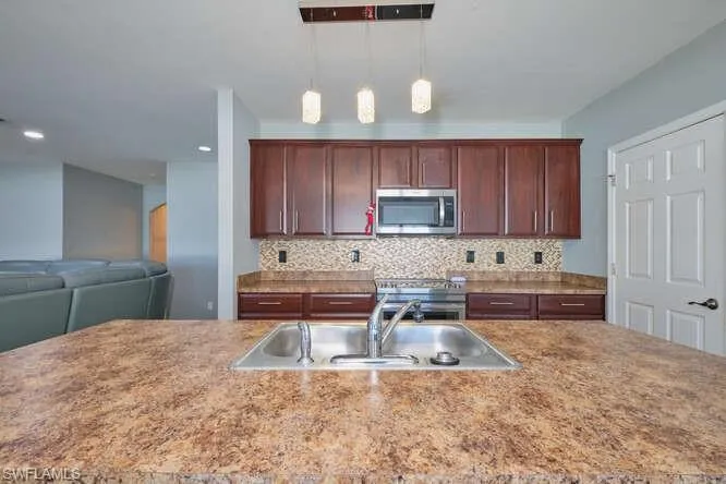 Kitchen with stainless steel appliances, tasteful backsplash, hanging light fixtures, an island with sink, and open floor plan