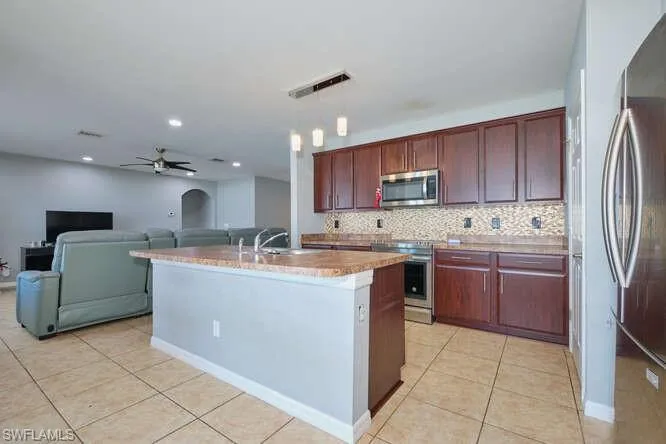 Kitchen featuring arched walkways, stainless steel appliances, hanging light fixtures, and light tile patterned floors