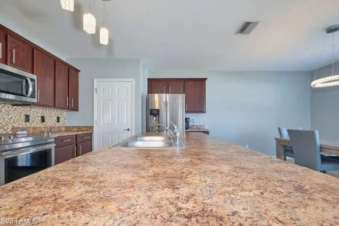 Kitchen with hanging light fixtures, appliances with stainless steel finishes, decorative backsplash, and dark brown cabinetry