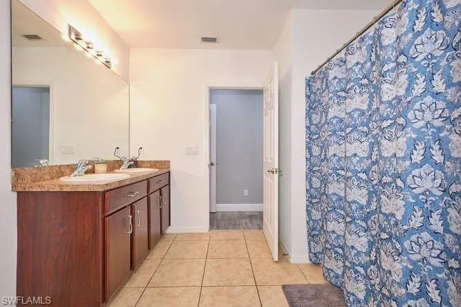 Bathroom with curtained shower, double vanity, and light tile patterned floors