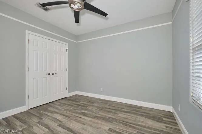 Unfurnished bedroom with dark wood-style floors, ceiling fan, a closet, and multiple windows