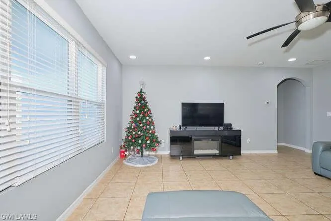 Living room with arched walkways, light tile patterned floors, ceiling fan, and recessed lighting