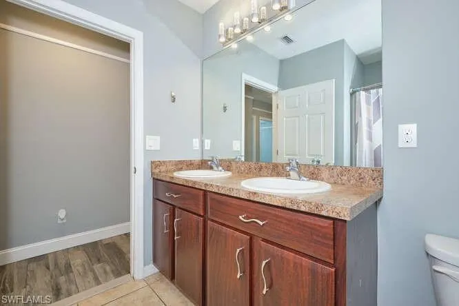 Full bath with curtained shower, double vanity, and light tile patterned floors