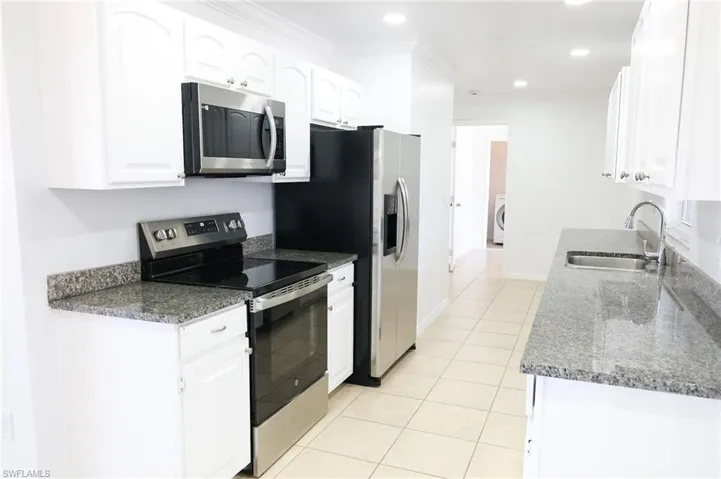 Kitchen featuring appliances with stainless steel finishes, dark stone counters, white cabinets, light tile patterned floors, and recessed lighting