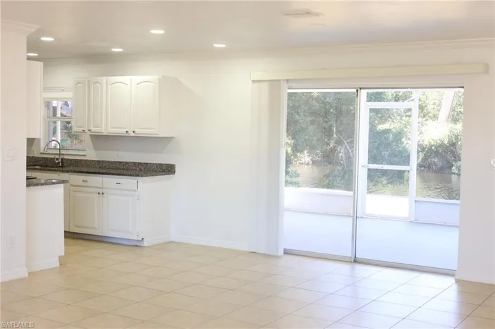 Kitchen with dark stone countertops, white cabinetry, ornamental molding, light tile patterned floors, and recessed lighting