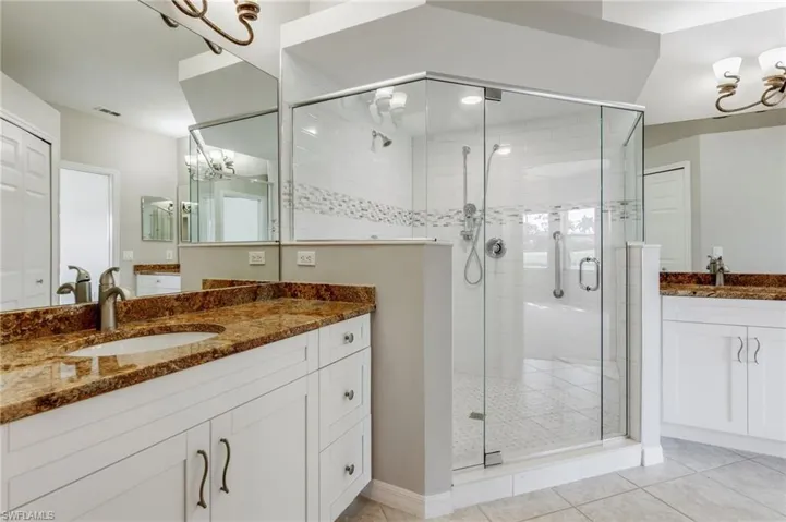 Bathroom featuring a chandelier, a stall shower, two vanities, and light tile patterned flooring