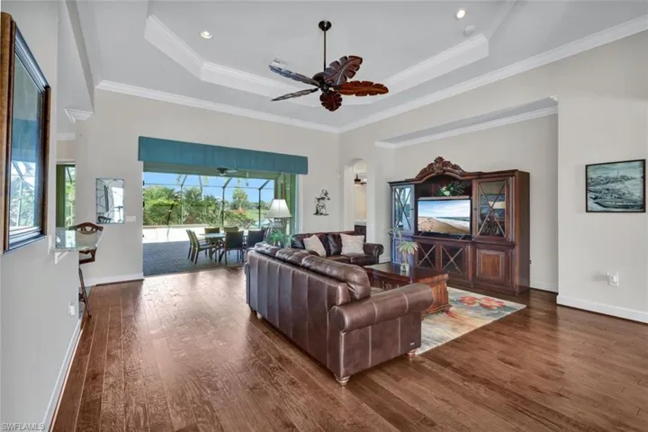 Living room with a raised ceiling, ceiling fan, dark hardwood / wood-style flooring, and ornamental molding